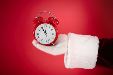 Photo of Santa Claus holding alarm clock on red background, closeup. Christmas countdown