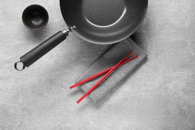 Empty iron wok, sauce bowl and chopsticks on grey table, flat lay