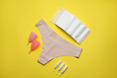 Photo of Flat lay composition with woman's panties and menstrual hygiene products on yellow background