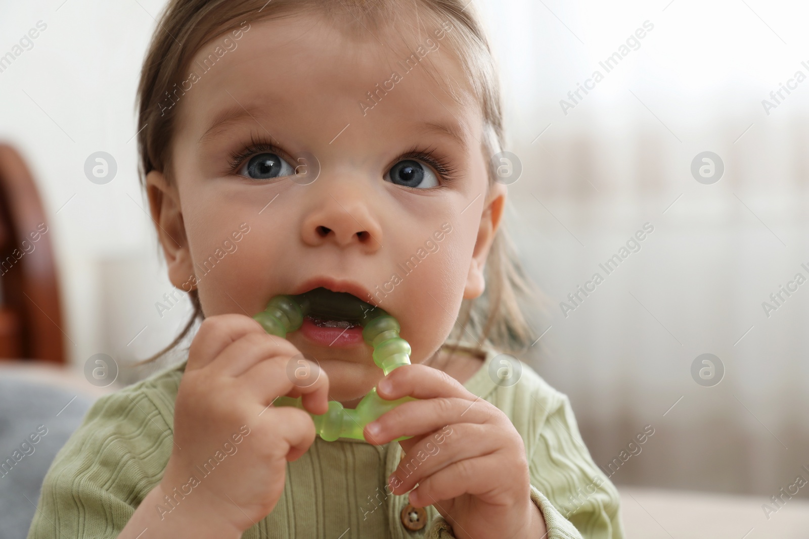 Photo of Cute baby girl with teething toy at home, closeup