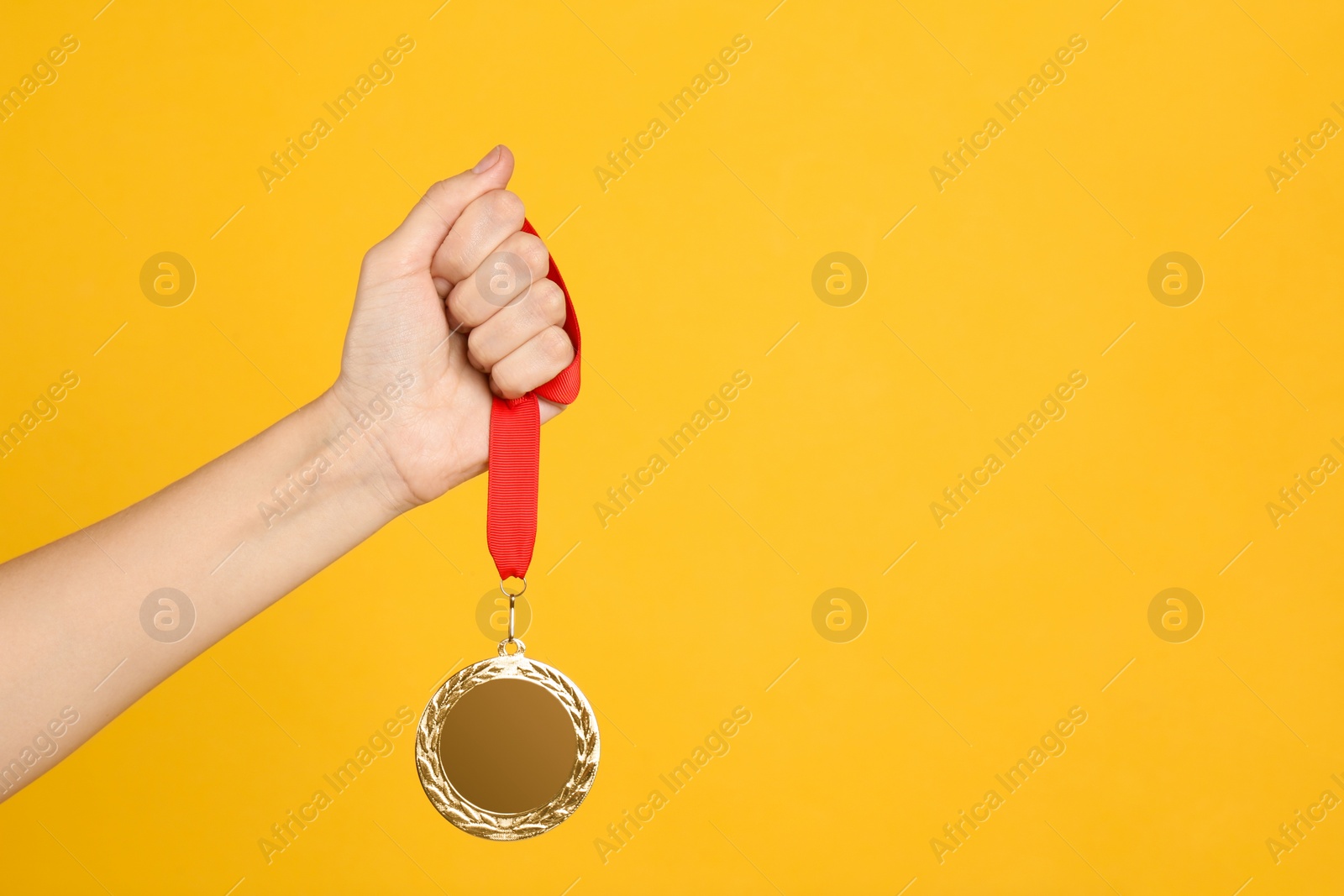 Photo of Woman holding golden medal on yellow background, closeup. Space for design