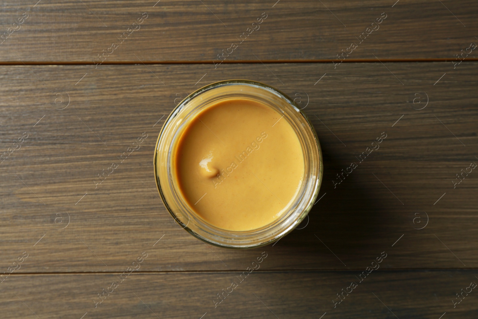 Photo of Spicy mustard in glass jar on wooden table, top view