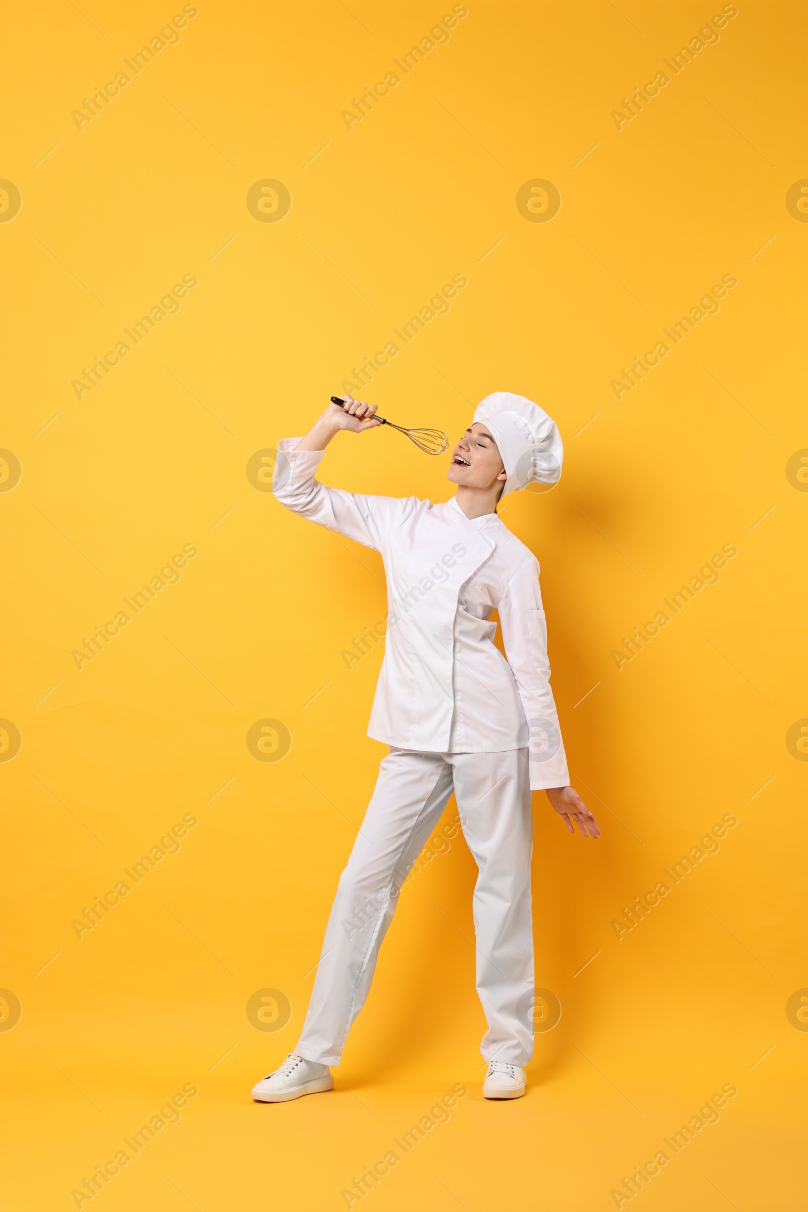 Photo of Professional chef with whisk having fun on yellow background