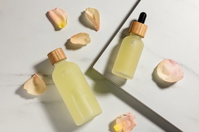 Photo of Bottles of essential oil and flower petals on white marble table, flat lay