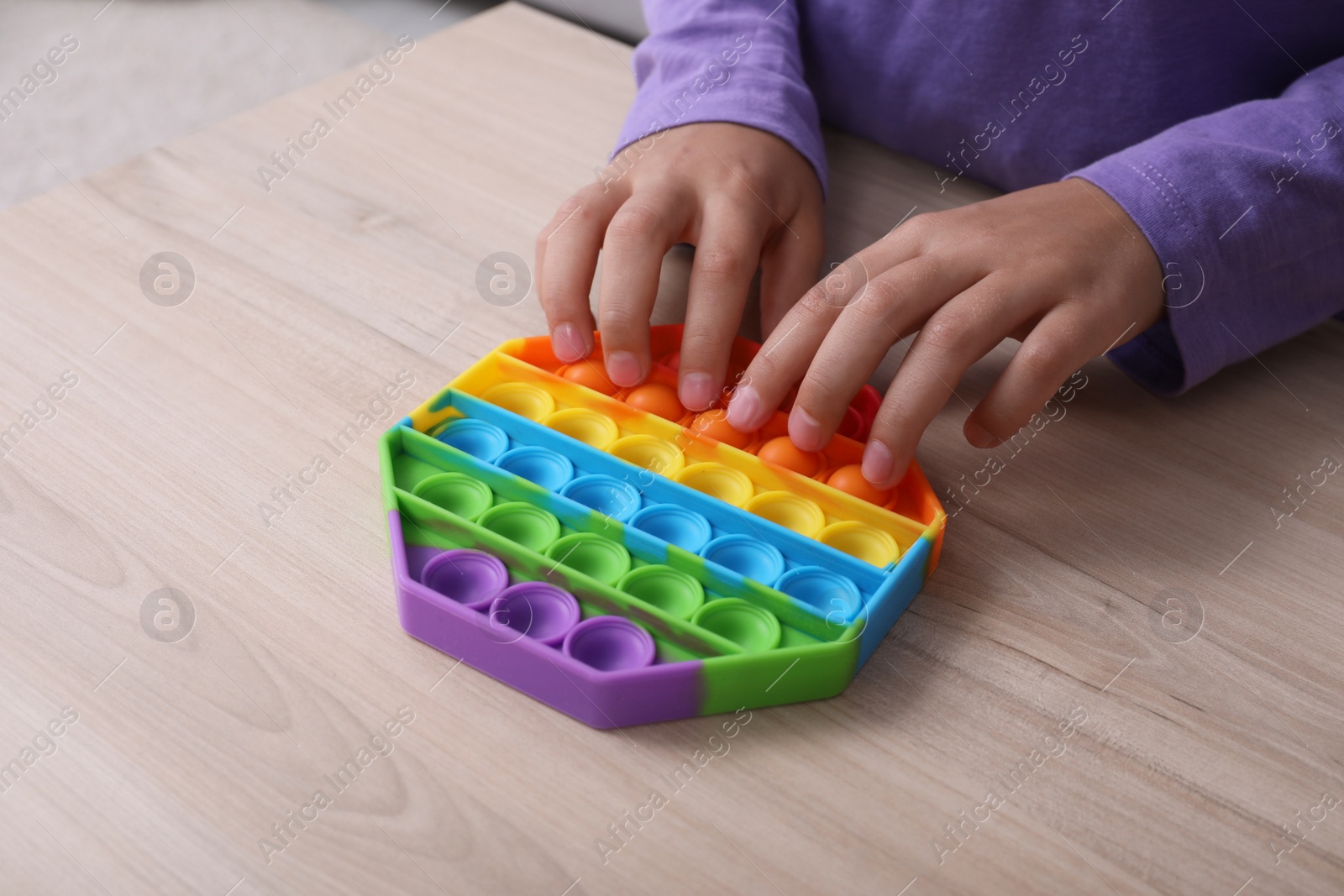 Photo of Little child playing with pop it fidget toy at wooden table, closeup