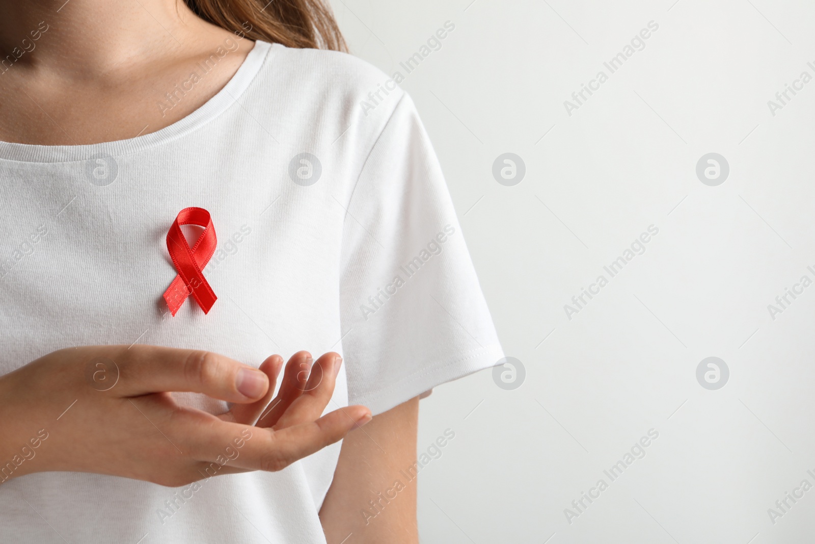 Photo of Woman with red ribbon on t-shirt against light background. Cancer awareness