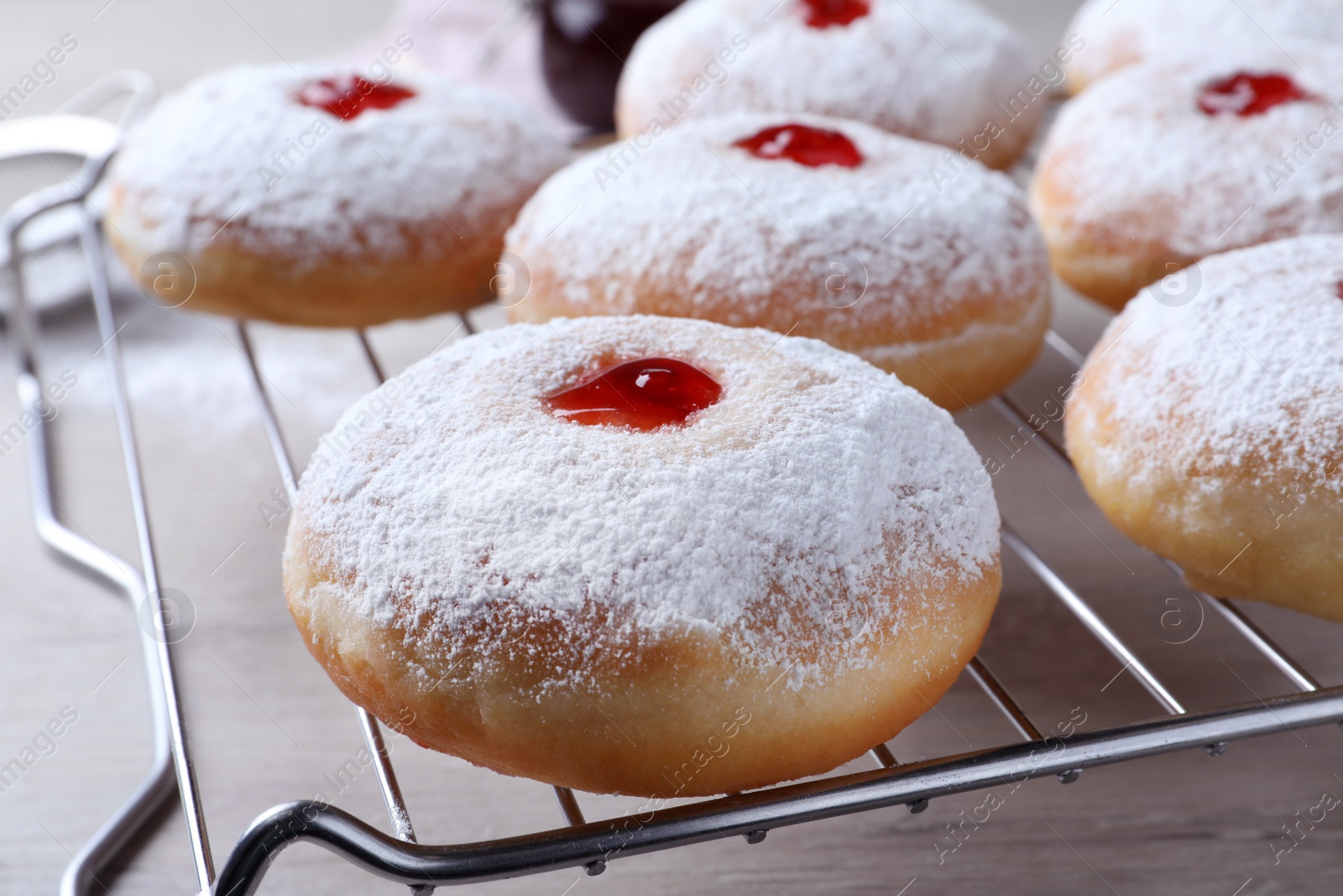 Photo of Many delicious donuts with jelly and powdered sugar on cooling rack, closeup