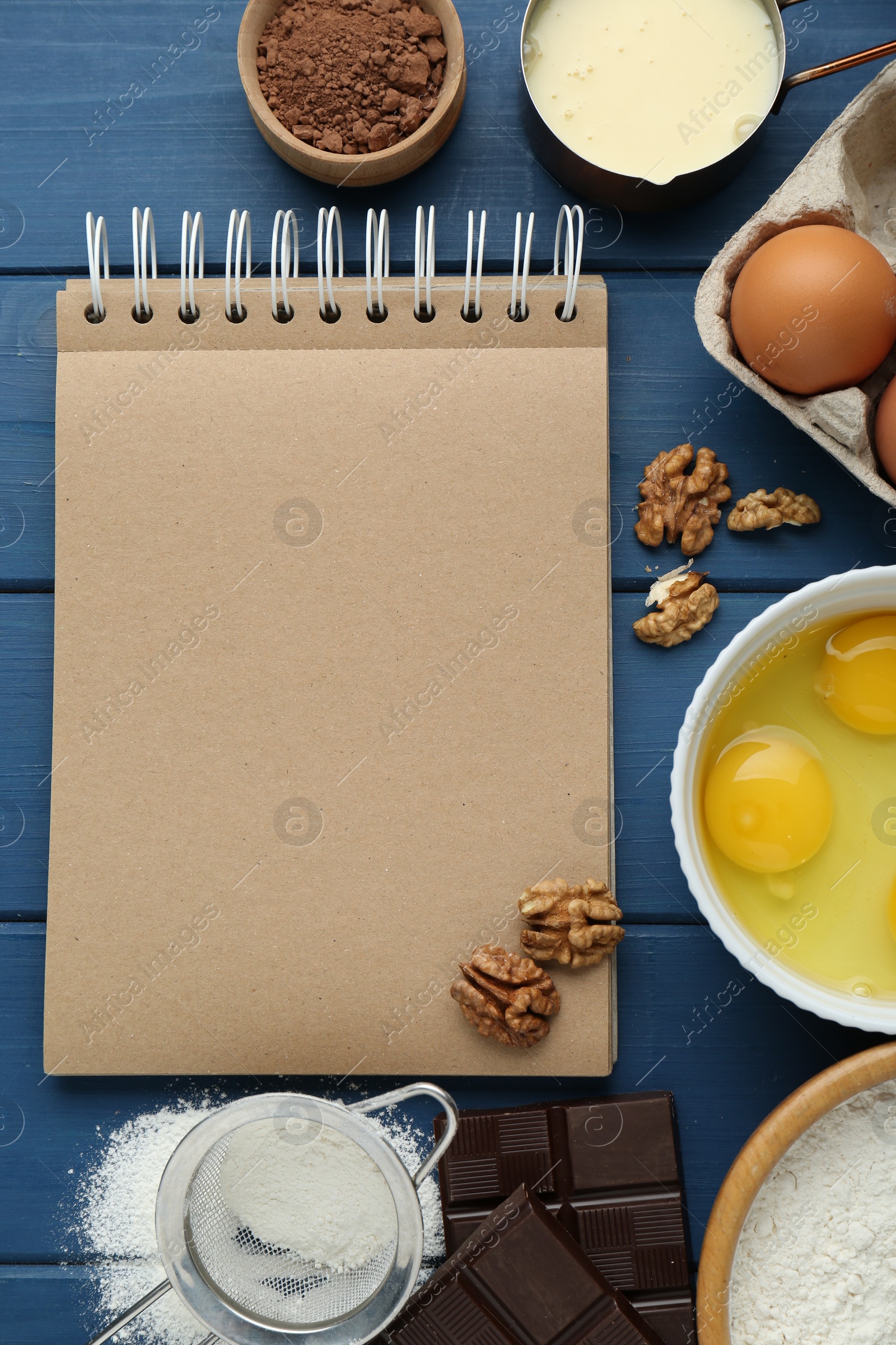 Photo of Blank recipe book and different ingredients on blue wooden table, flat lay. Space for text