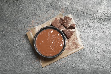 Tasty milk chocolate paste in bowl and pieces on gray table, top view