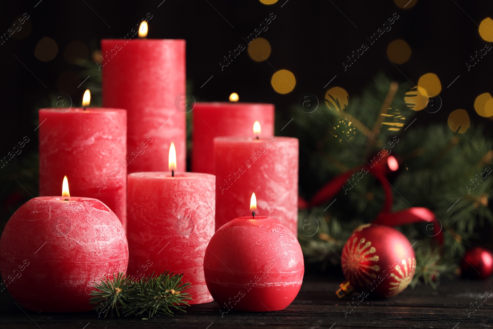 Photo of Burning red candles with Christmas decor on table against blurred lights