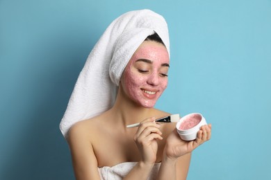Photo of Woman applying pomegranate face mask on light blue background