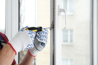 Photo of Construction worker adjusting installed window with screwdriver indoors, closeup