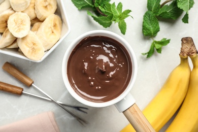 Photo of Fondue pot with milk chocolate and bananas on light table, top view