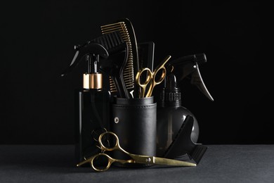 Different hairdresser tools on grey table against black background