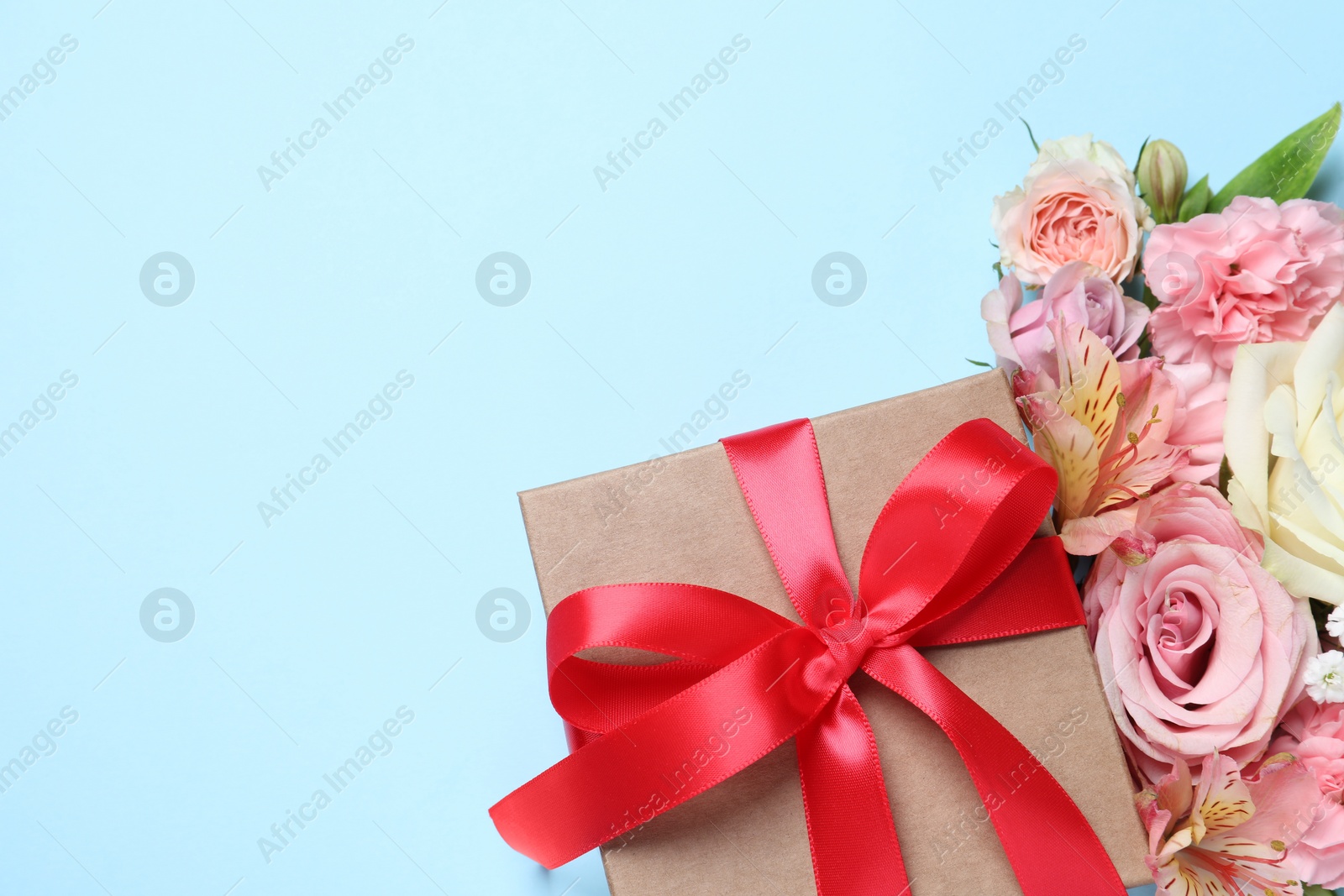 Photo of Gift box and beautiful flowers on light blue background, flat lay. Space for text