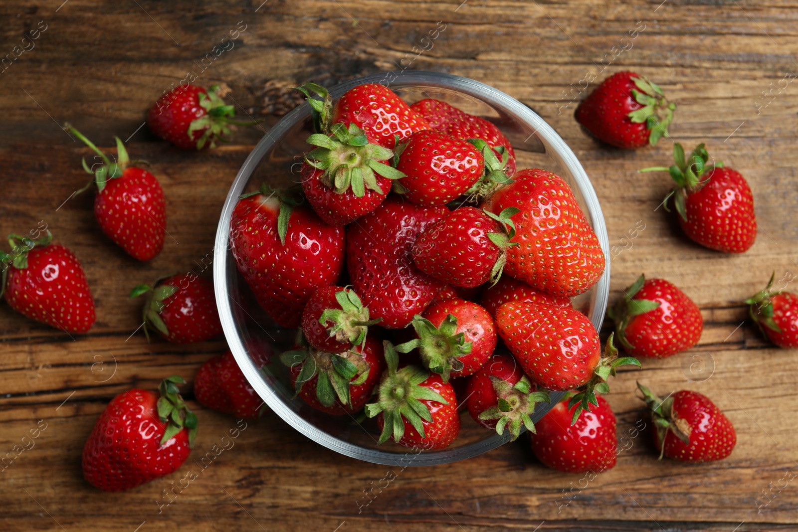 Photo of Delicious ripe strawberries in glass bowl on wooden table, flat lay