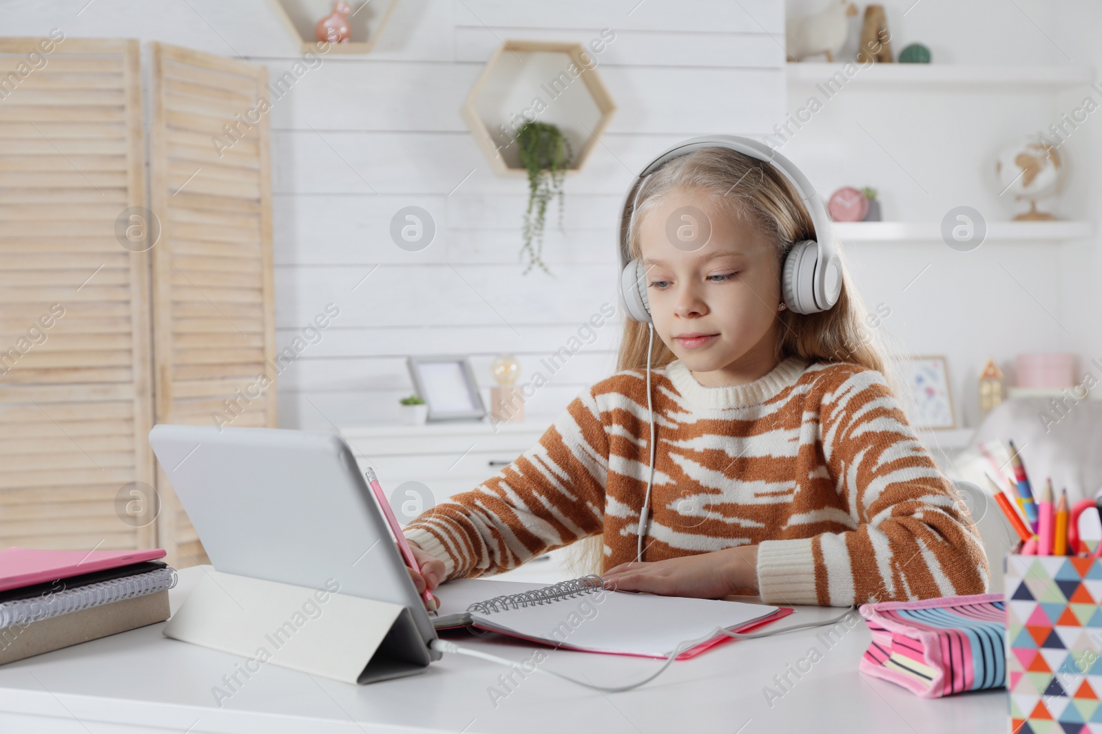 Photo of Cute little girl with modern tablet studying online at home. E-learning