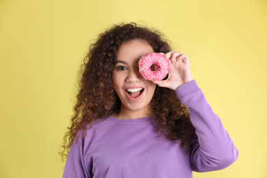 Beautiful African-American woman with donut on yellow background