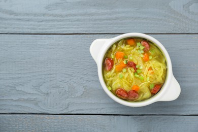 Delicious sauerkraut soup with smoked sausages and green onion on grey wooden table, top view. Space for text
