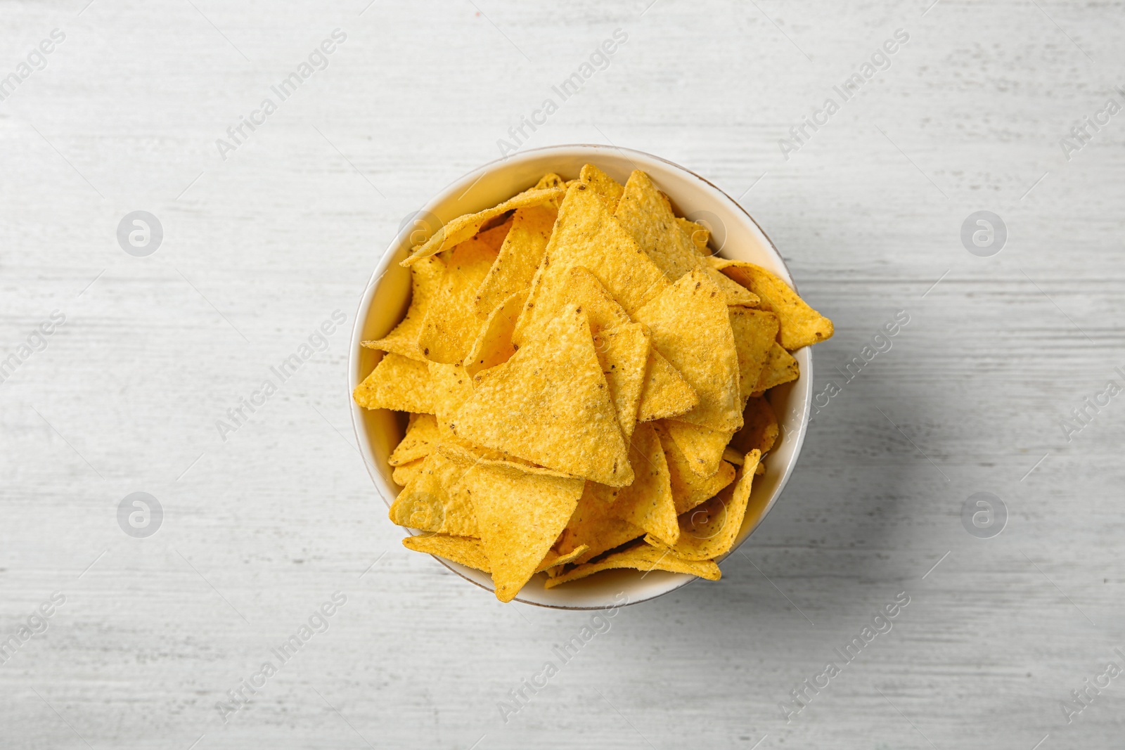 Photo of Tasty mexican nachos chips in bowl on white wooden table, top view