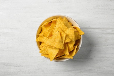 Photo of Tasty mexican nachos chips in bowl on white wooden table, top view