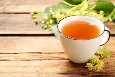 Photo of Cup of tea and linden blossom on wooden table. Space for text