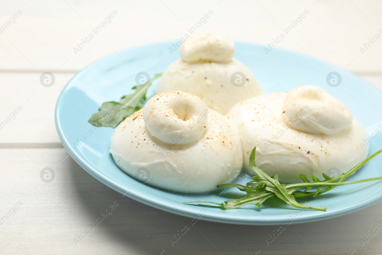 Photo of Delicious burrata cheese with arugula on white wooden table, closeup