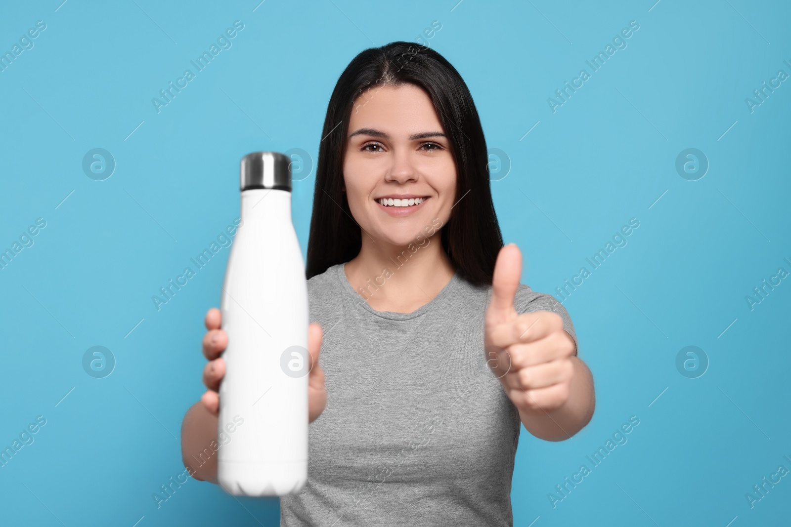 Photo of Young woman with thermo bottle on light blue background