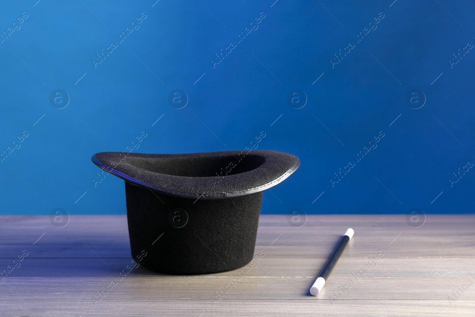 Photo of Magician's hat and wand on wooden table against blue background