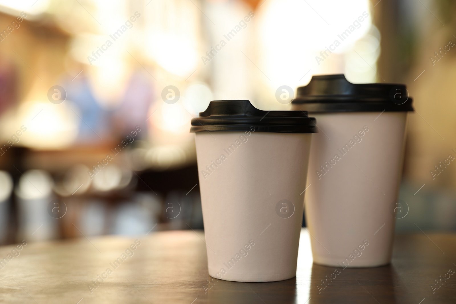 Photo of Cardboard takeaway coffee cups with plastic lids on wooden table in outdoor cafe, space for text