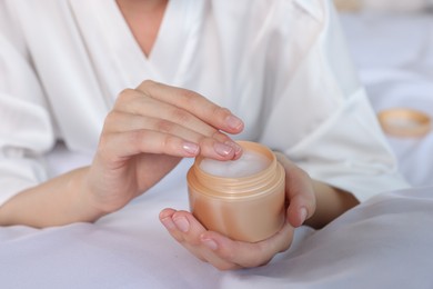 Photo of Woman taking hand cream from jar indoors, closeup