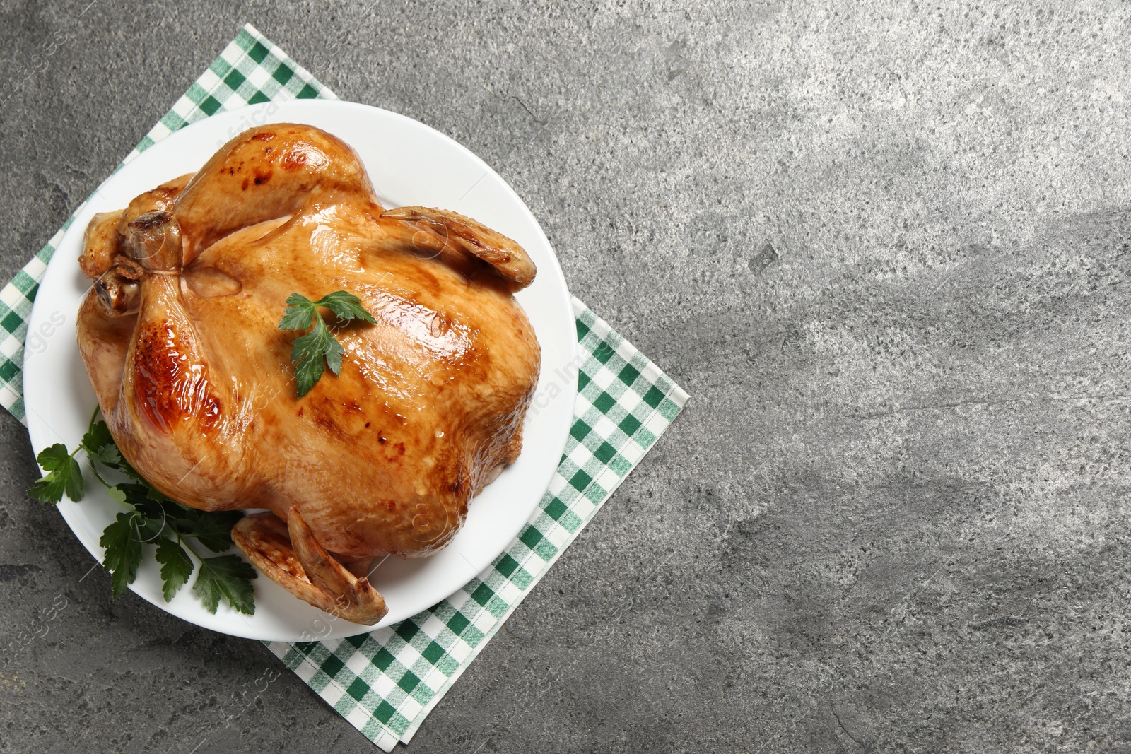 Photo of Tasty roasted chicken with parsley on grey textured table, top view. Space for text