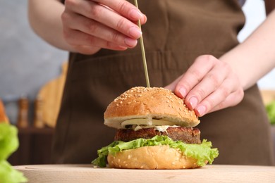 Photo of Woman making delicious vegetarian burger at table, closeup