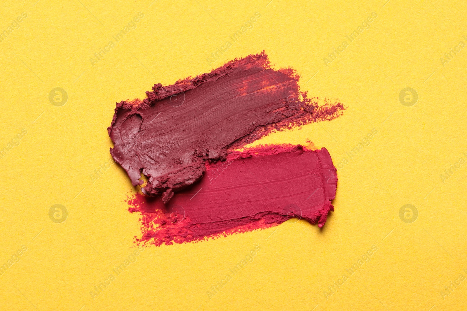 Photo of Smears of bright lipsticks on yellow background, top view