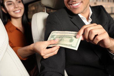 Photo of Young woman giving money taxi driver in modern car, closeup
