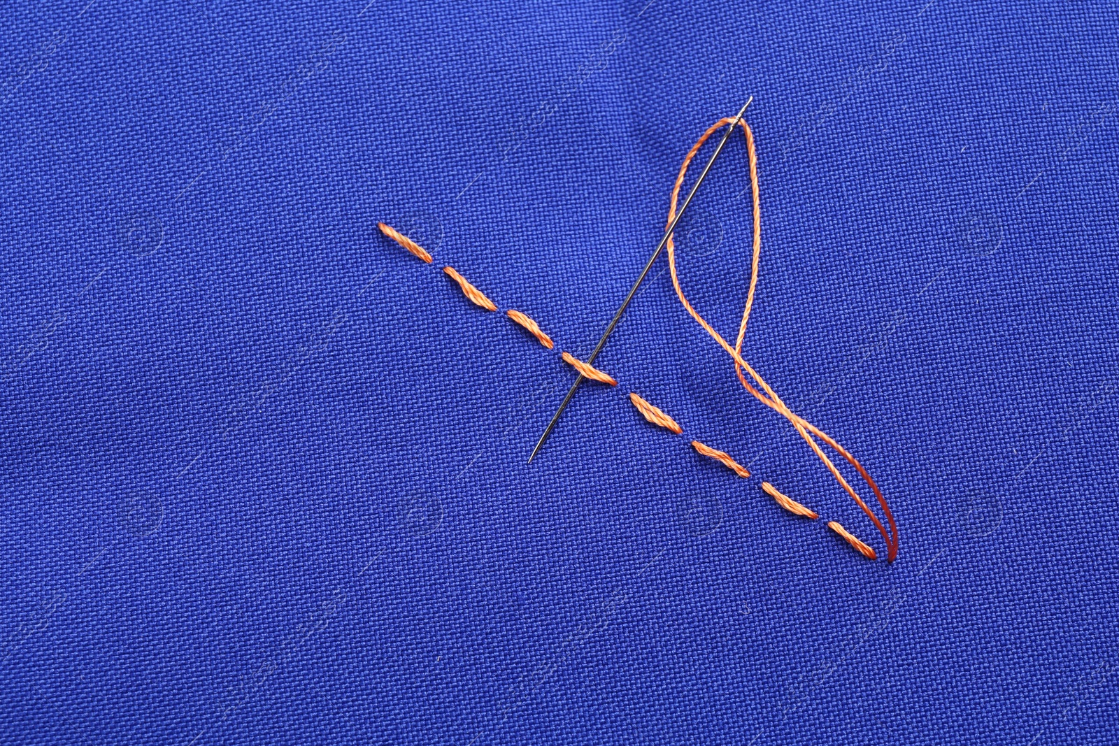 Photo of Sewing needle with thread and stitches on blue cloth, top view