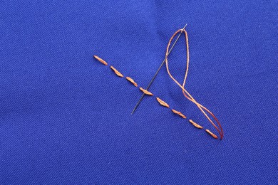 Sewing needle with thread and stitches on blue cloth, top view