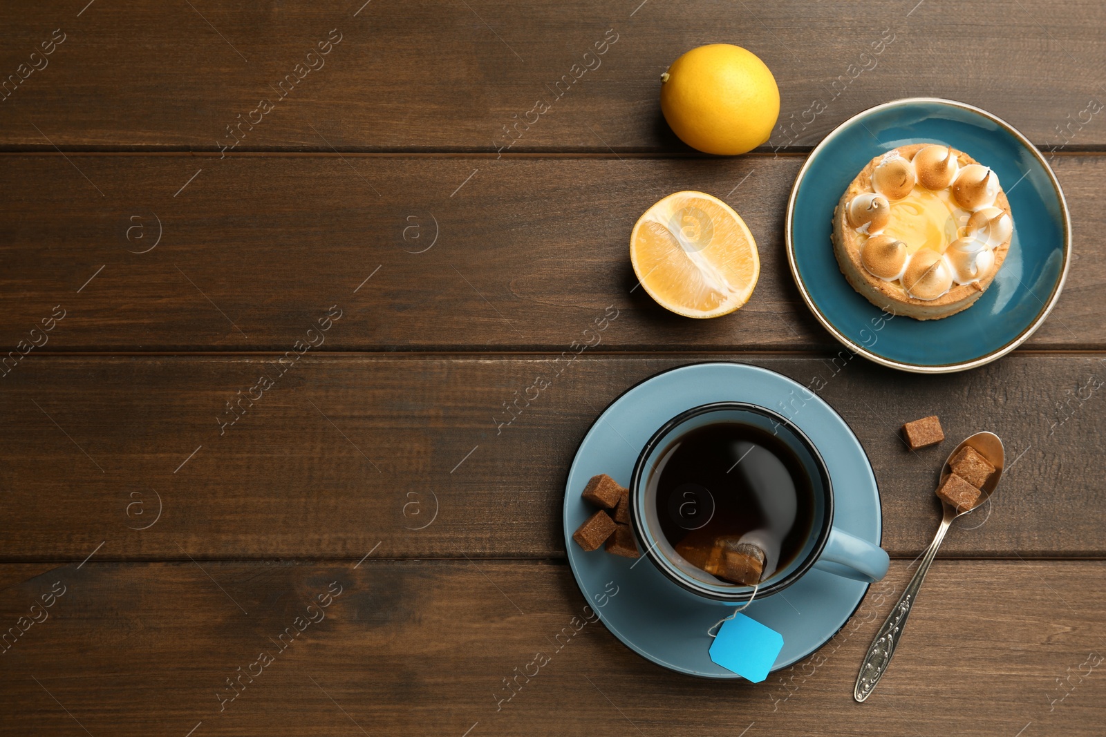 Photo of Tea bag in ceramic cup of hot water, dessert and sugar cubes on wooden table, flat lay. Space for text