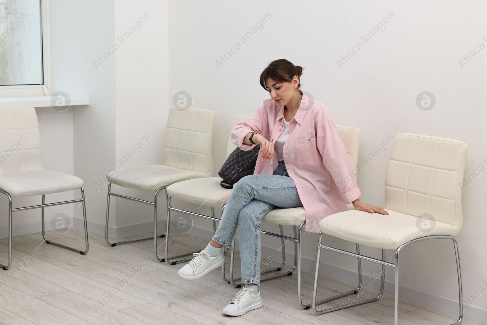 Photo of Woman looking at wrist watch and waiting for job interview indoors