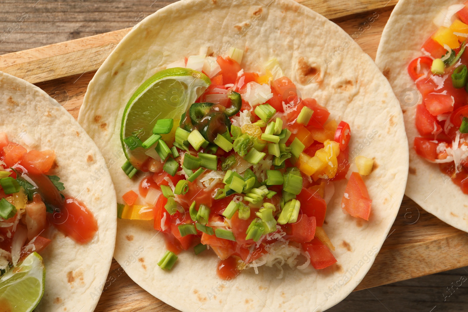 Photo of Delicious tacos with vegetables, green onion, lime and ketchup on wooden table, top view