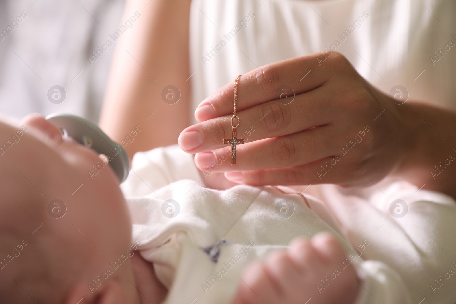 Photo of Mother holding Christian cross near newborn baby indoors, focus on hand