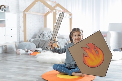 Cute little girl playing with cardboard armor in bedroom