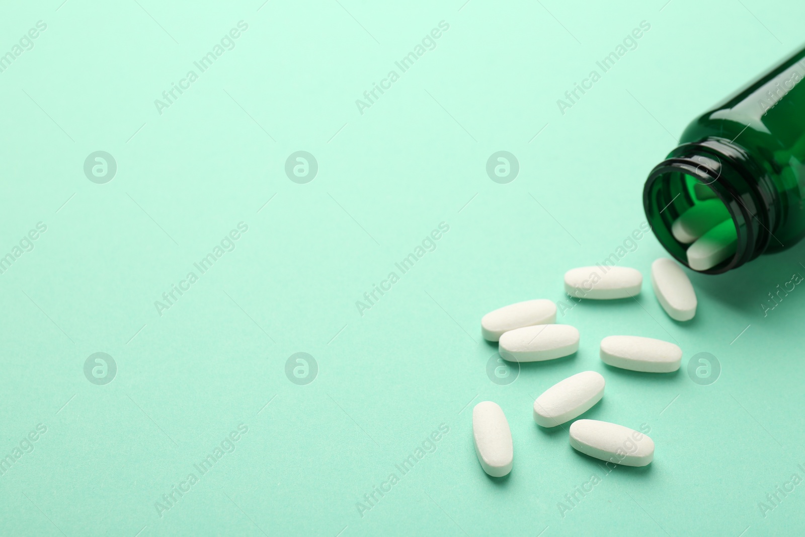 Photo of Vitamin pills and bottle on mint color background. Space for text