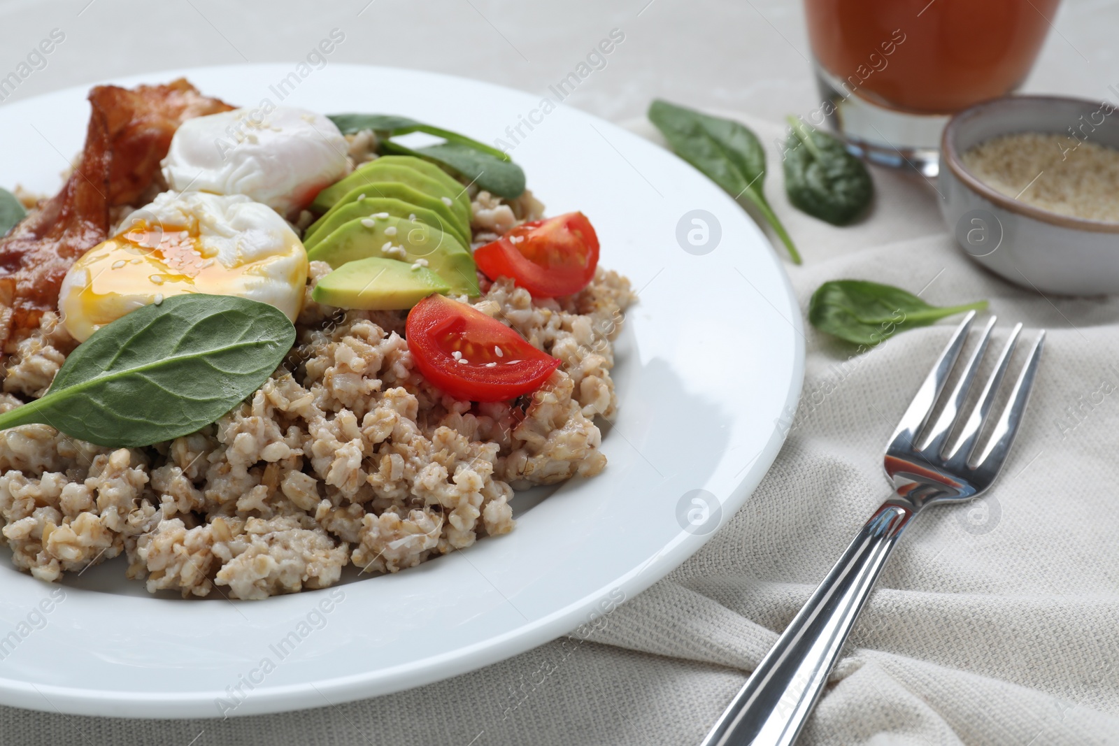 Photo of Delicious boiled oatmeal with poached egg, bacon, avocado and tomato served on table, closeup