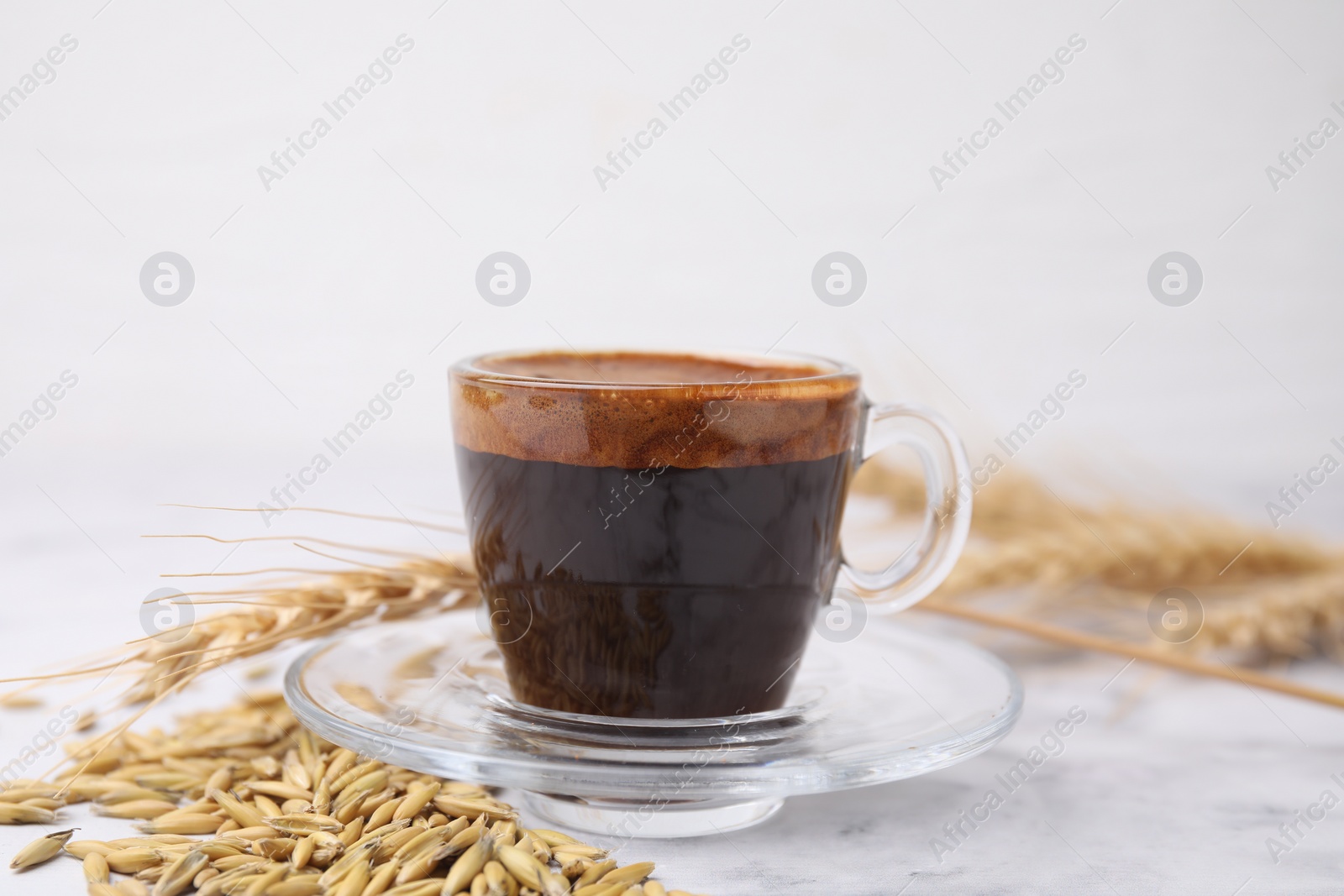 Photo of Cup of barley coffee, grains and spike on light table, closeup