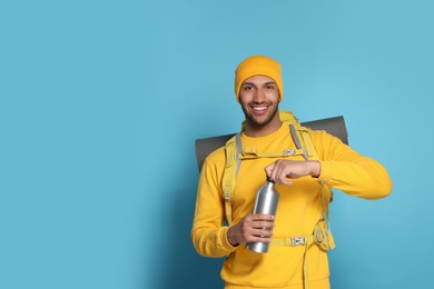 Photo of Happy tourist with backpack and thermo bottle on light blue background, space for text
