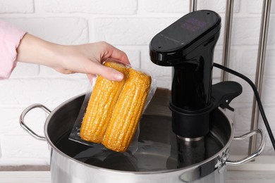 Photo of Woman putting vacuum packed corn into pot, closeup. Sous vide cooking