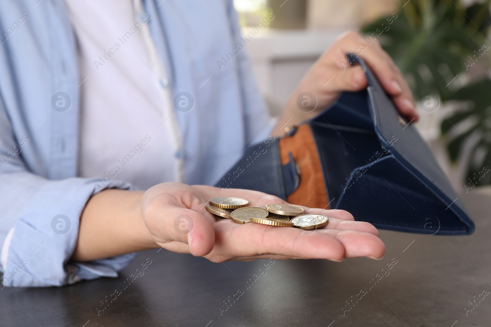 Photo of Poor woman holding coins and empty wallet at grey table indoors, closeup