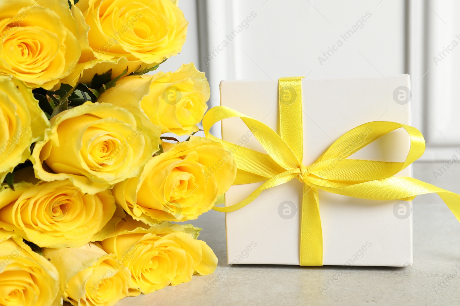 Photo of Beautiful bouquetyellow roses and gift box on light grey table, closeup