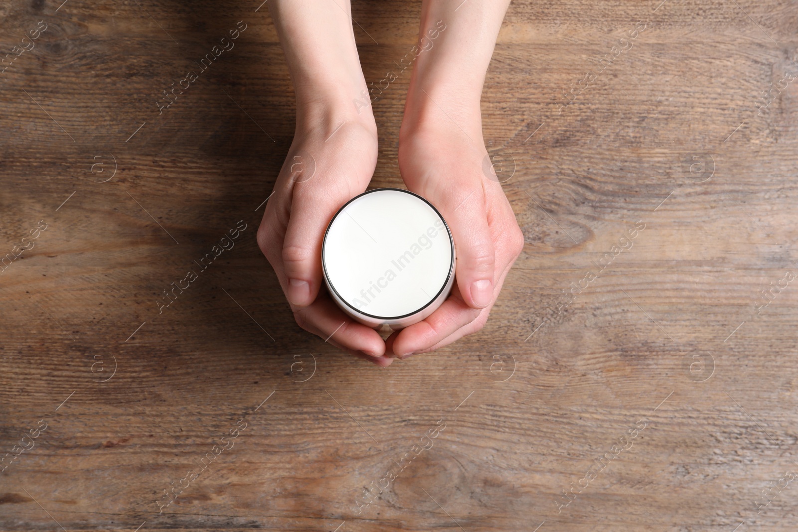 Photo of Woman holding glass of milk at wooden table, top view